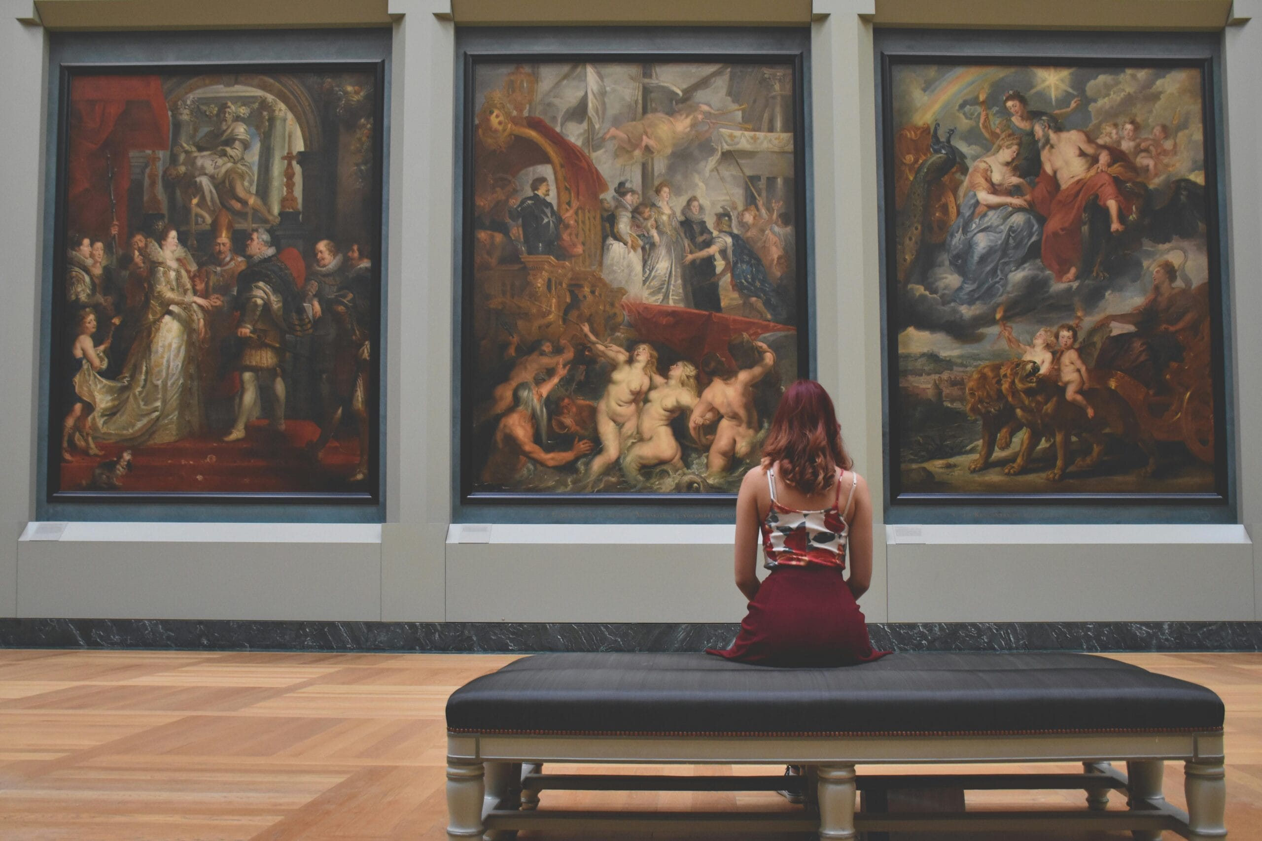 Museum: Woman Sitting on Ottoman in Front of Three Paintings